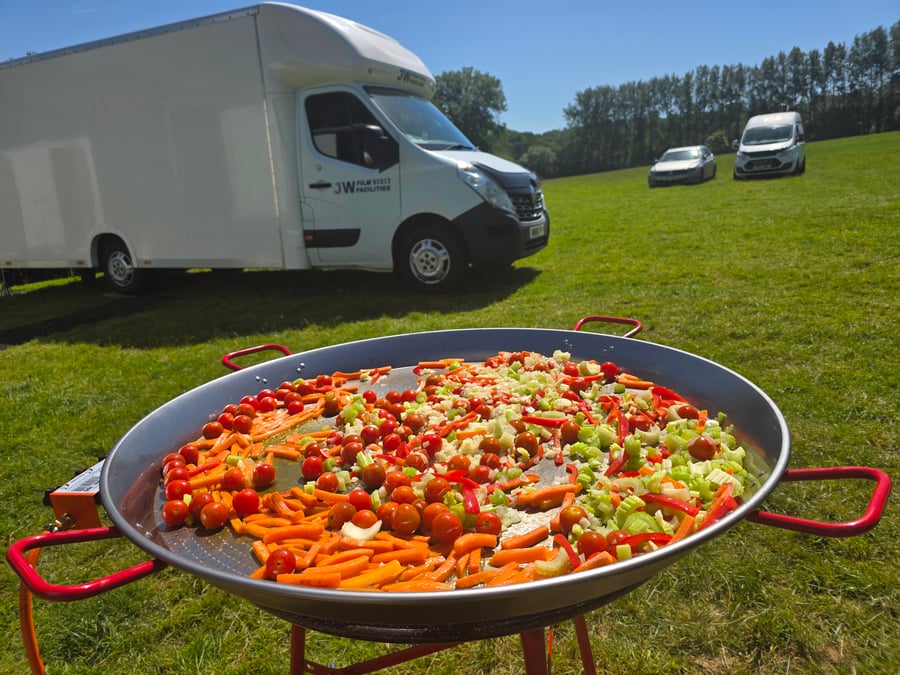 A giant paella pan filled with colourful vegetables cooking outdoors at a film production unit base on a sunny day