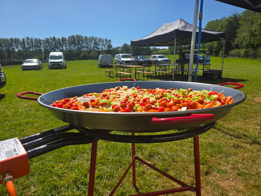 A giant paella pan filled with colourful vegetables, ready to be cooked outdoors on a sunny day