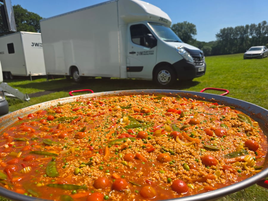 A vibrant giant paella cooking outdoors at a film or TV production unit base on a sunny day