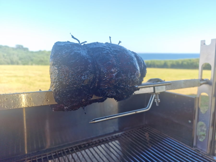 A whole hog roast slowly cooking on a spit with a beautiful coastal view in the background