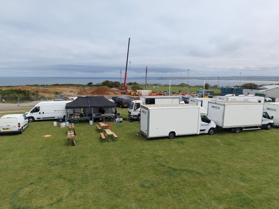 A film and TV crew catering setup with a marquee, tables, and production vehicles on a grassy field by the coast