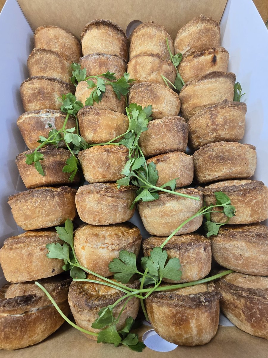 A box of golden-crusted savoury pies, garnished with fresh parsley, ready for a buffet