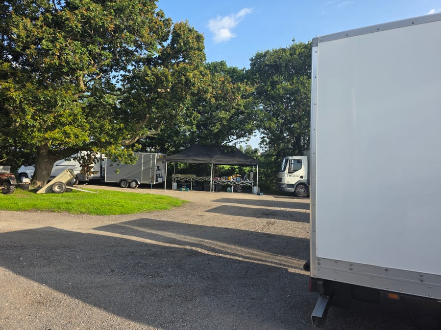 A film or TV production unit base with catering setup under a gazebo, surrounded by vehicles and trees