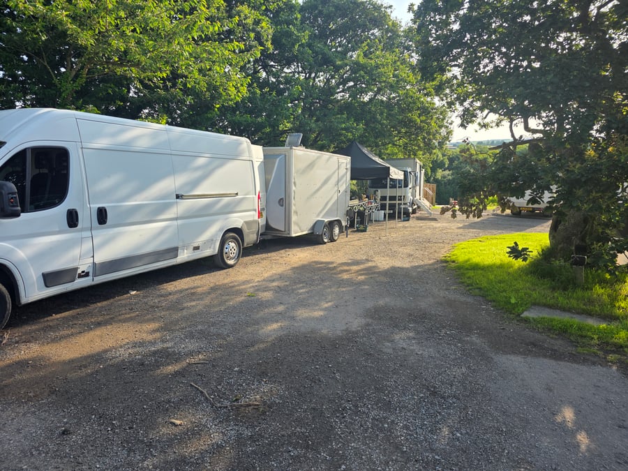 A catering van and trailer at a film or TV production unit base, with a glimpse of the catering setup under a gazebo