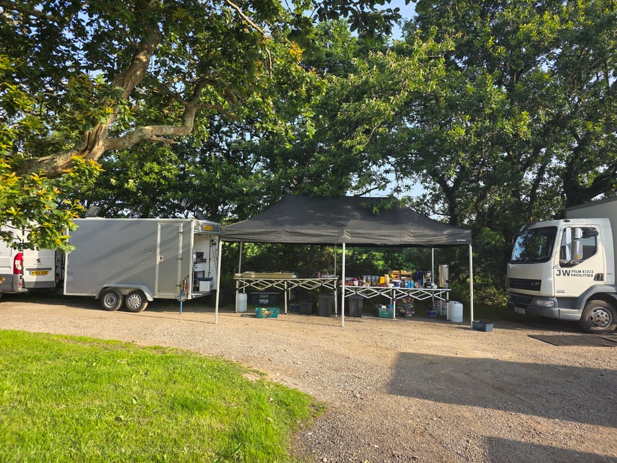 A catering setup with a gazebo, tables, and vehicles at a film or TV production unit base