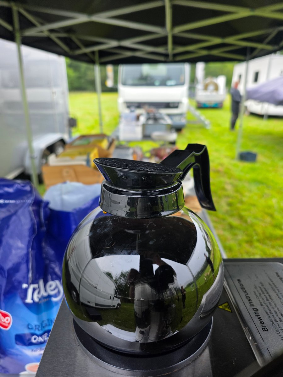 A coffee pot on a catering setup at a film or TV production unit base, with vehicles and a gazebo in the background
