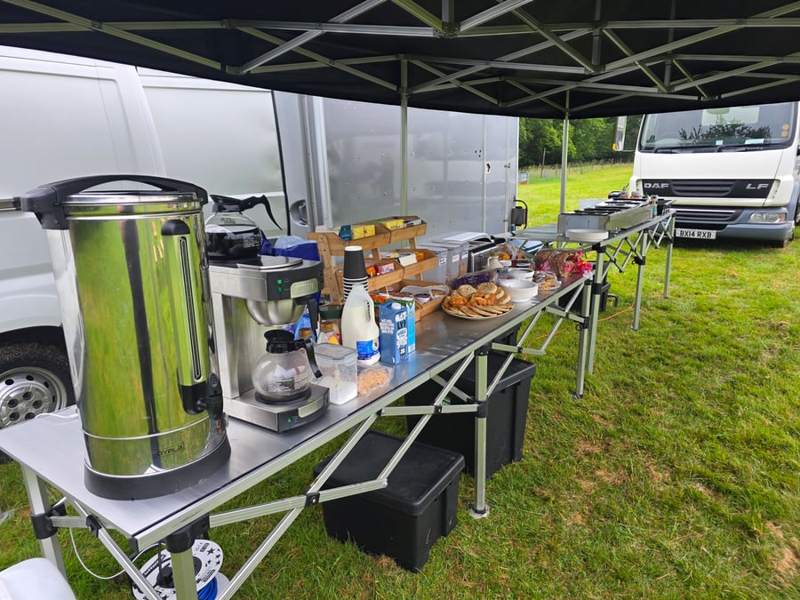 A breakfast buffet with hot drinks and pastries set up under a gazebo at a film or TV production unit base