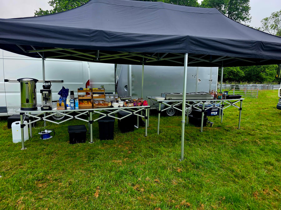 A catering setup under a gazebo with hot drinks, snacks, and cooking equipment, likely for a film or TV crew