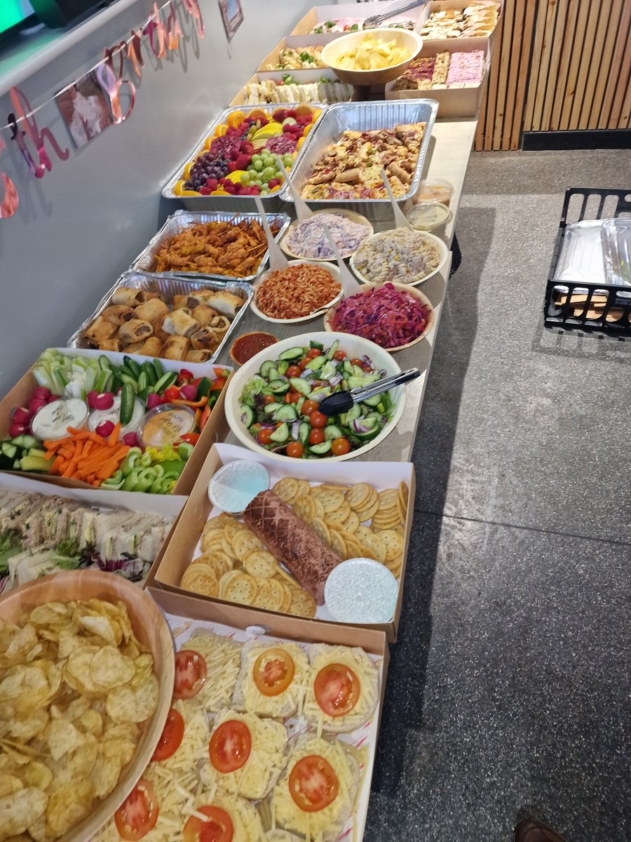 A long buffet table laden with various food platters including sandwiches, fruit, and salads