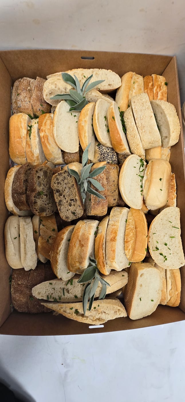 A cardboard box filled with a variety of sliced bread and rolls, garnished with herbs