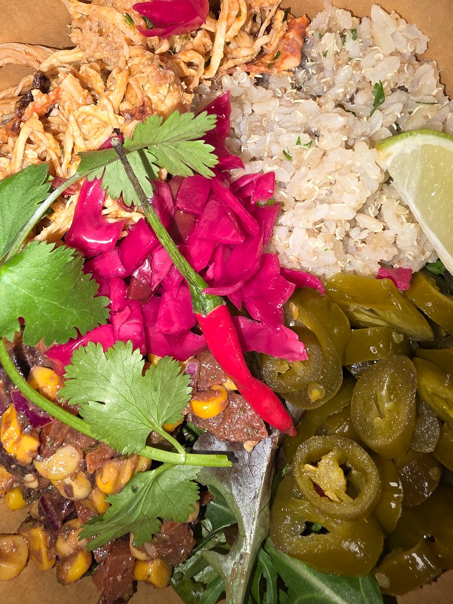 A close-up of a vibrant platter with pulled pork, rice, jalapenos, and pickled cabbage