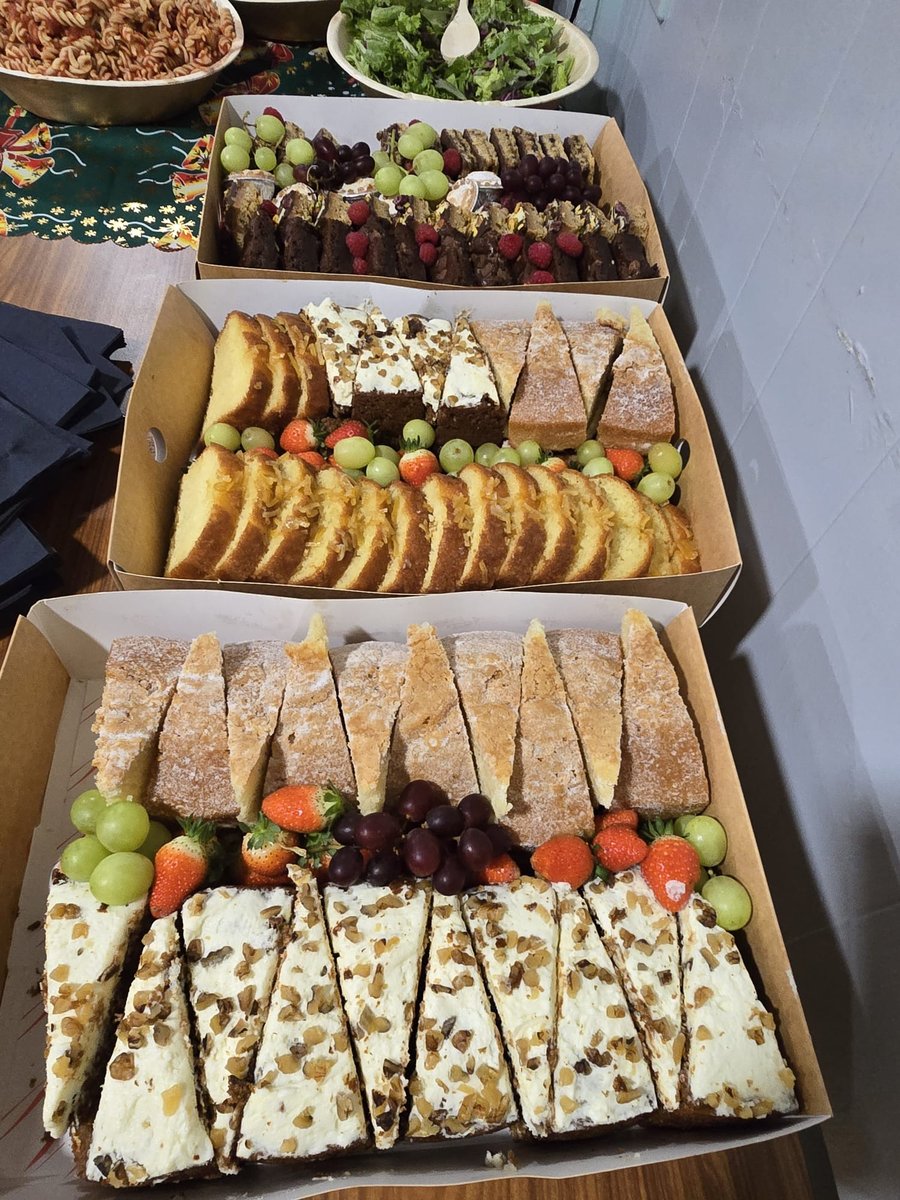 Assortment of sliced cakes and fruit arranged in catering boxes