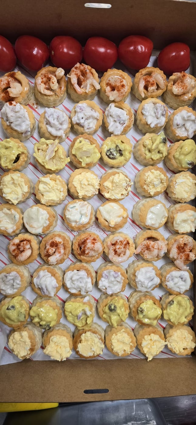 A box of assorted vol-au-vents with various fillings and whole tomatoes