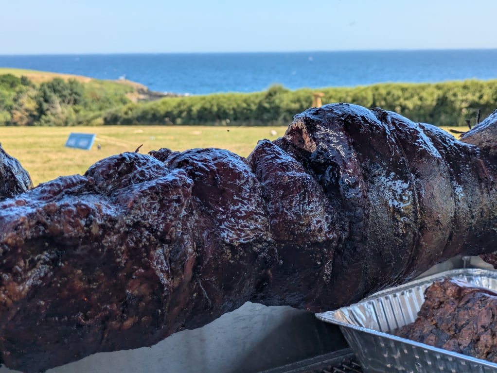 Hog roast on spit with Cornish coastal backdrop