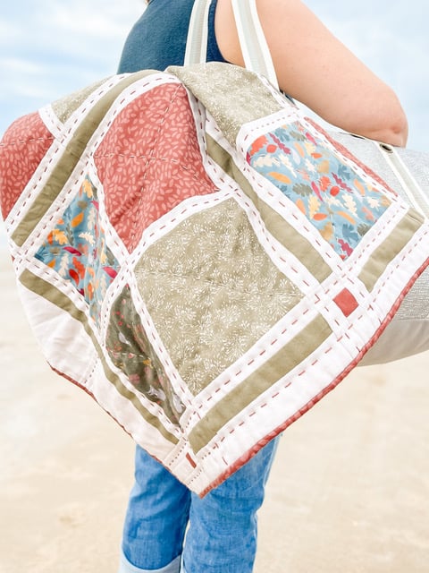 a lady on a beach holding a made from one of fold and sews no cut quilt kits with organic sateen quilting fabric 