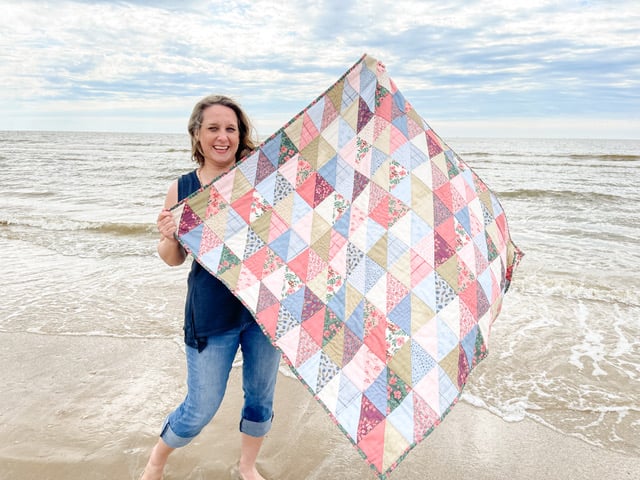 danea boquet, founder of Fold&sew on a beach holding one of her quilts made with a no-cut quilt kit