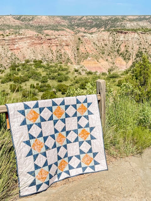 a beautiful navy and orange quilt pattern from fold&sew quilts hanging over a wooden railing near a canyon