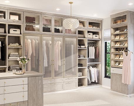 Custom walk in closet design with extra shelving, shoe storage, island, lighted glass cabinets by California Closets