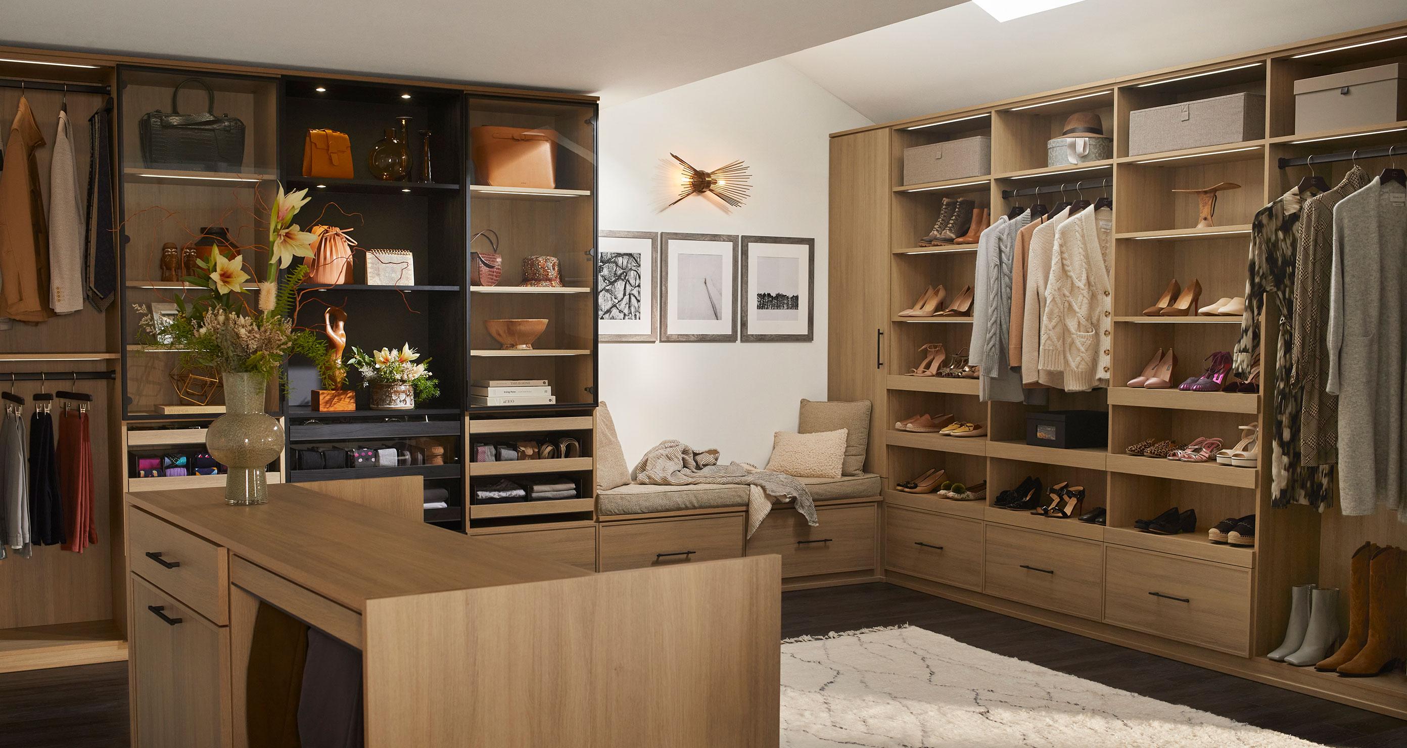 Large walk in closet with center island for accessories, with custom shelves, cabinets and drawers in light wood grain finish