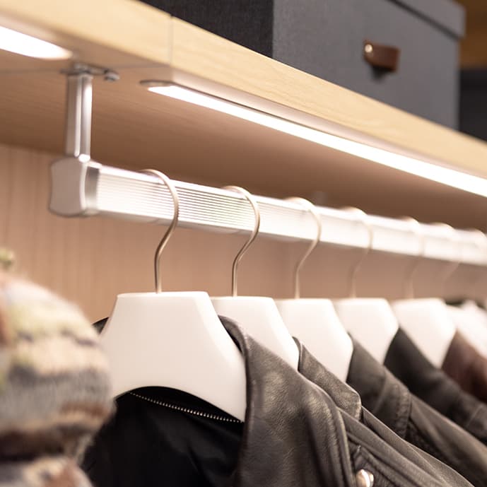 Customized LED ribbon lighting above hanging wardrobe rod in walk in closet by California Closets