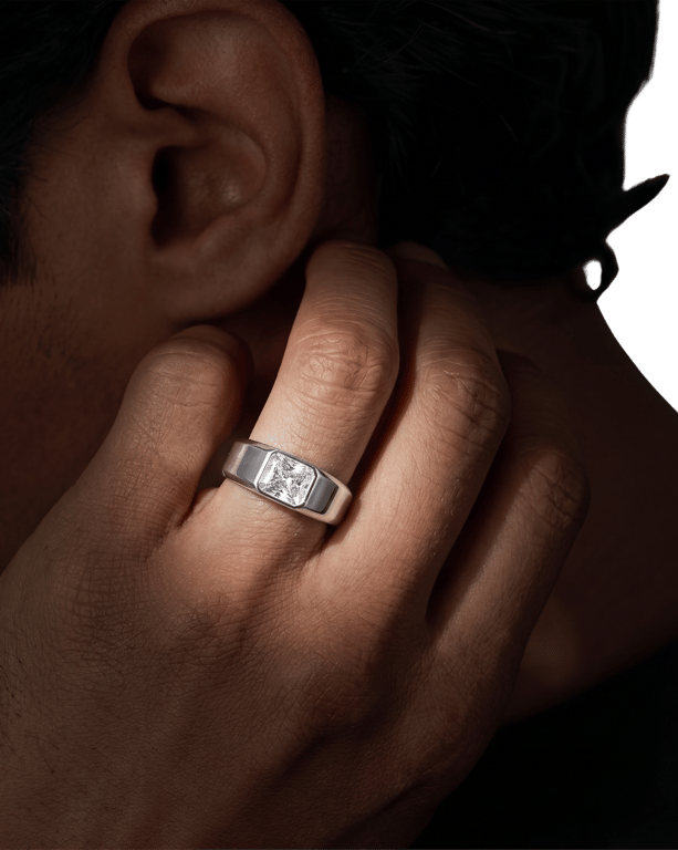 A diamond-set signet band, worn on a hand raised to the ear