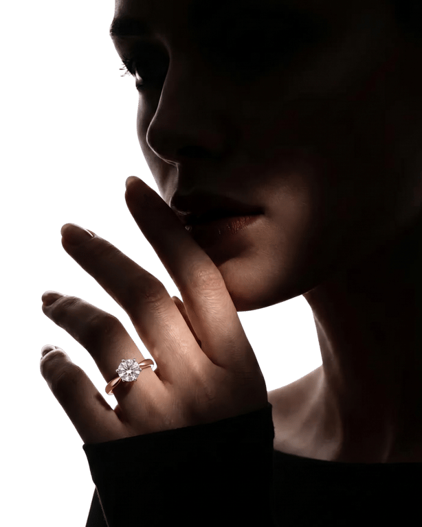 A rose-gold solitaire ring, worn on a hand raised to the lips