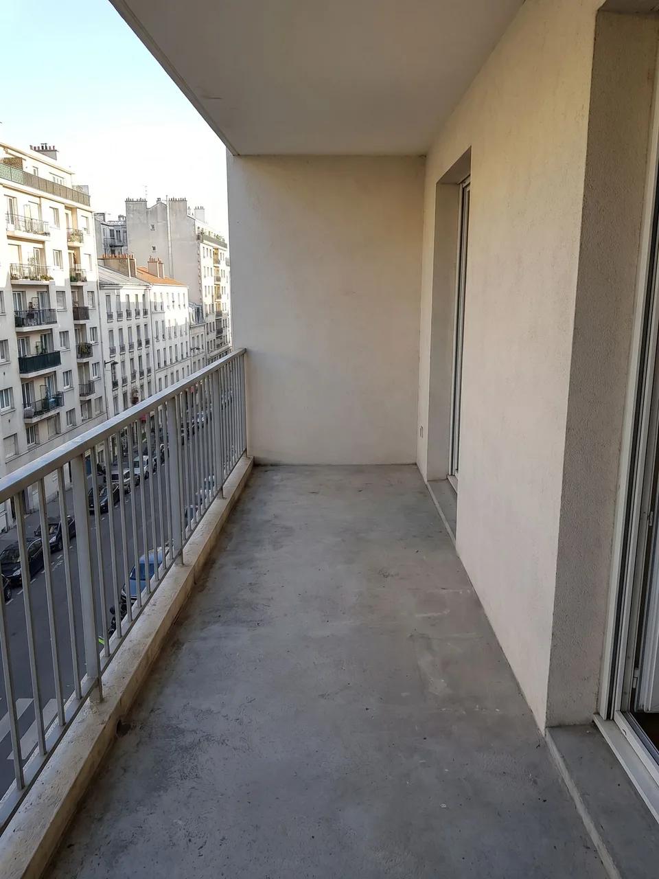 Long narrow city balcony with concrete floor, pale stucco walls, metal railing and sliding door to apartment