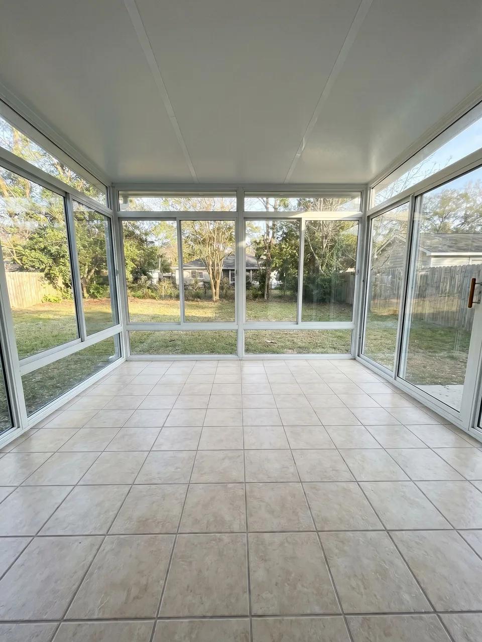 Empty sunroom with white window frames, tiled floor and sliding glass door looking out to backyard