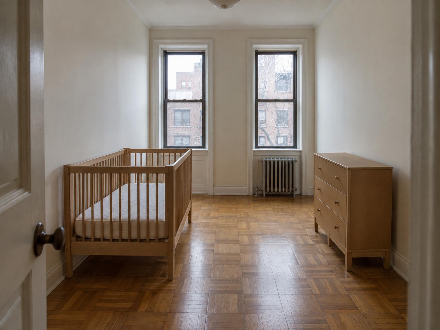Narrow nursery with two tall windows, parquet floor, wooden crib and three-drawer dresser under soft daylight.