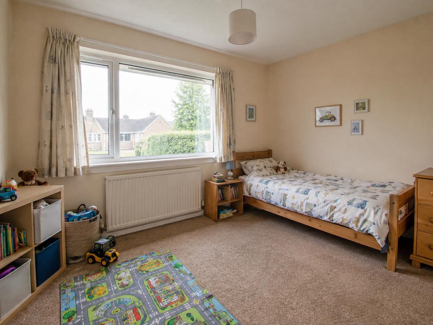 Small kids bedroom with large front window, pine single bed, cube storage and play rug on beige carpet.