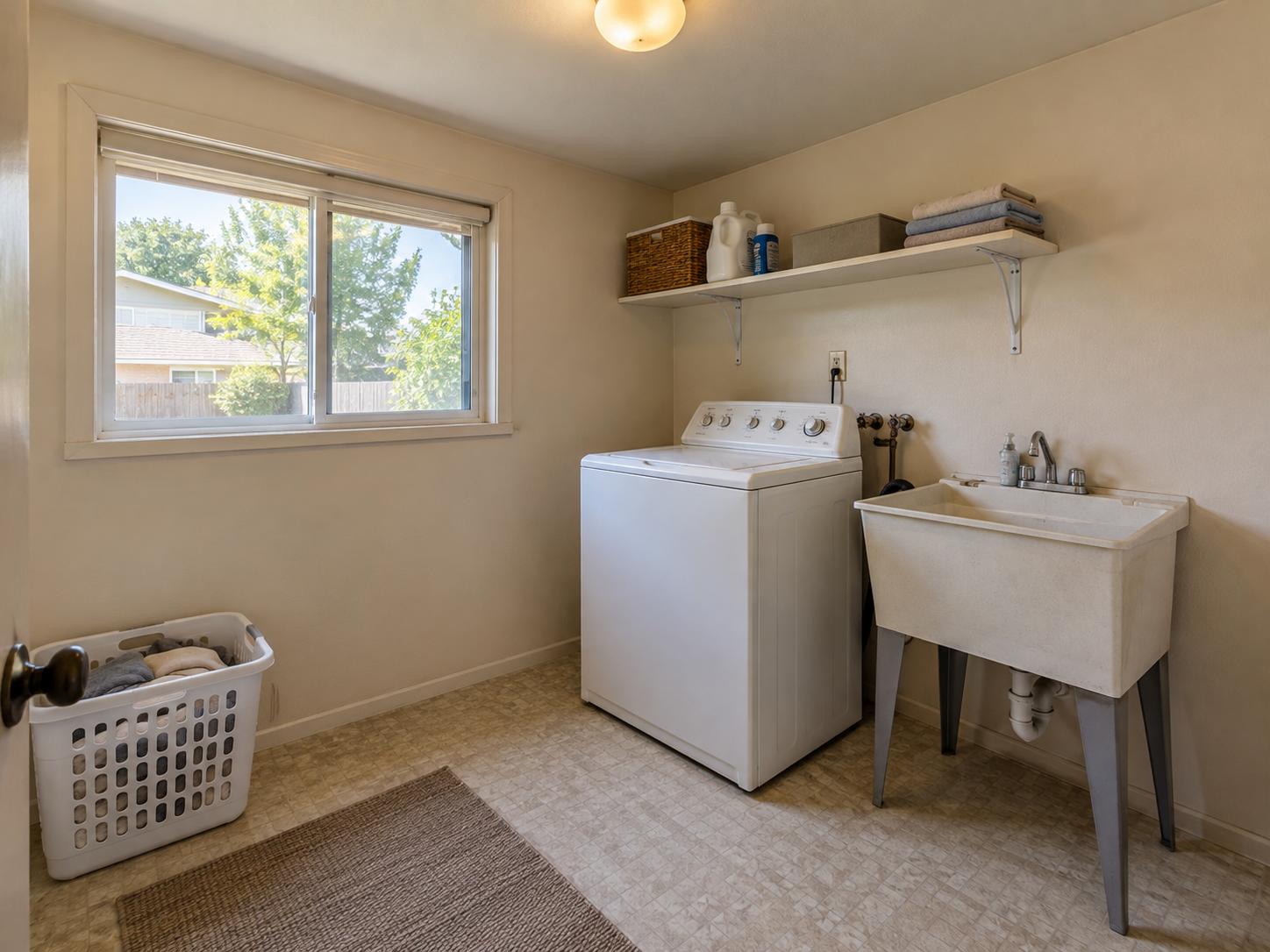 Compact laundry room with top-load washer, freestanding plastic utility sink, single white shelf and small window.