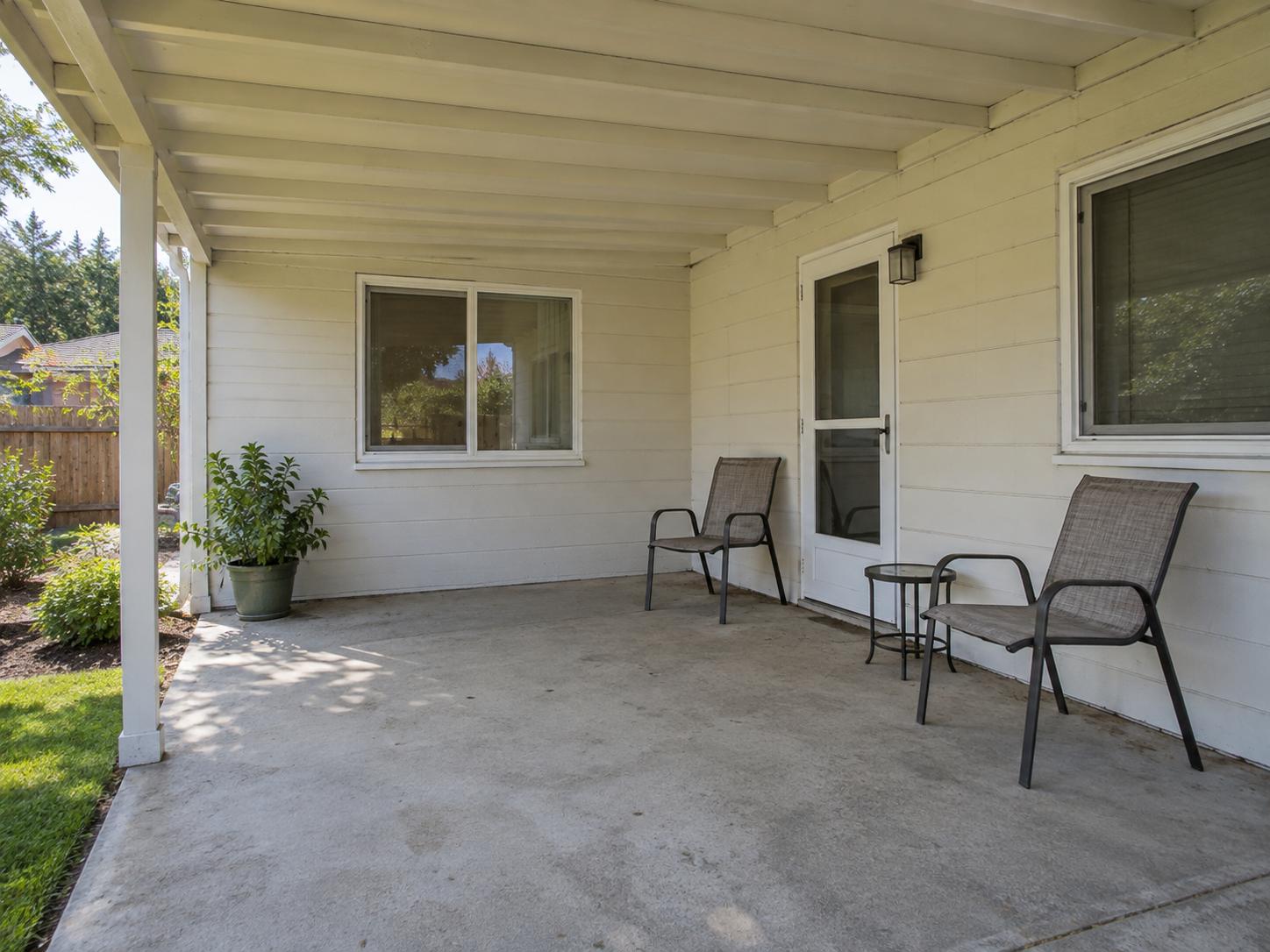 Covered patio with white siding, exposed roof beams, two metal sling chairs and concrete floor