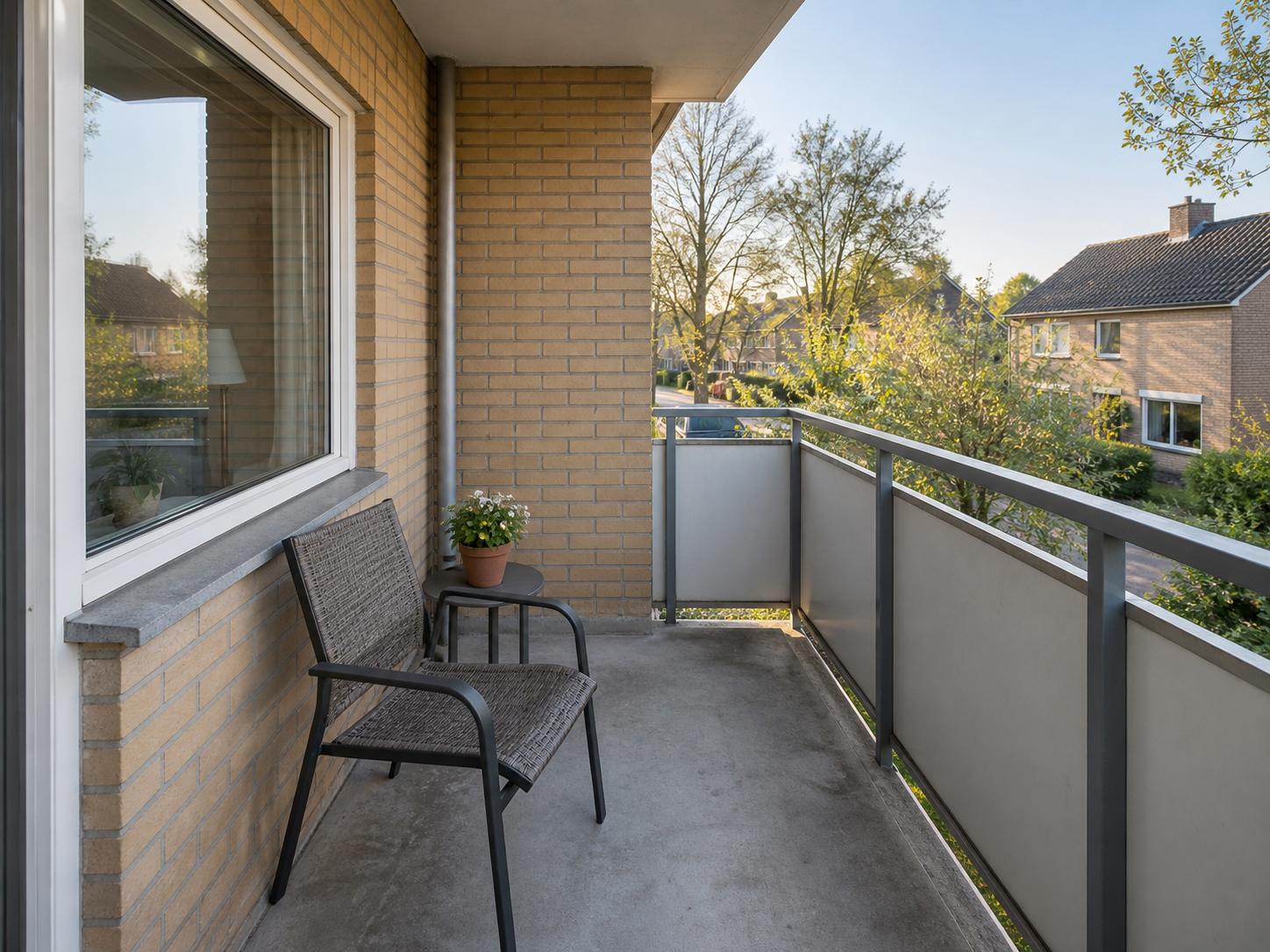 Narrow brick balcony with concrete floor, single metal-framed chair and small potted plant