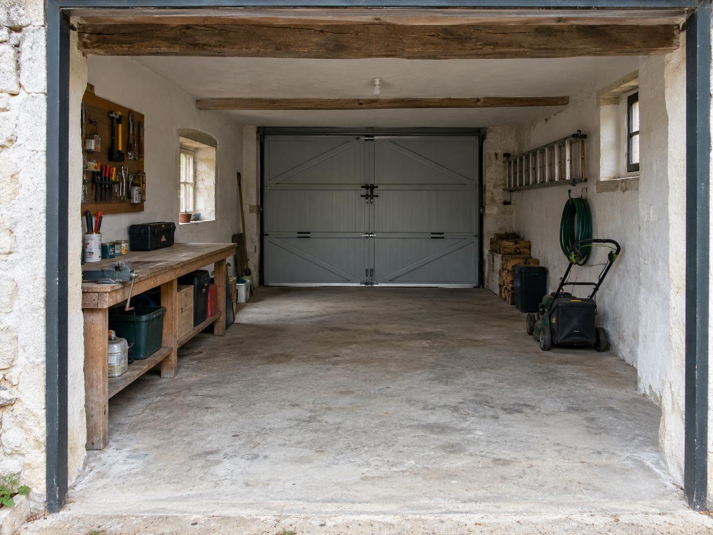 Rustic garage with wooden workbench left, exposed beams, concrete floor, ladder and lawnmower on right