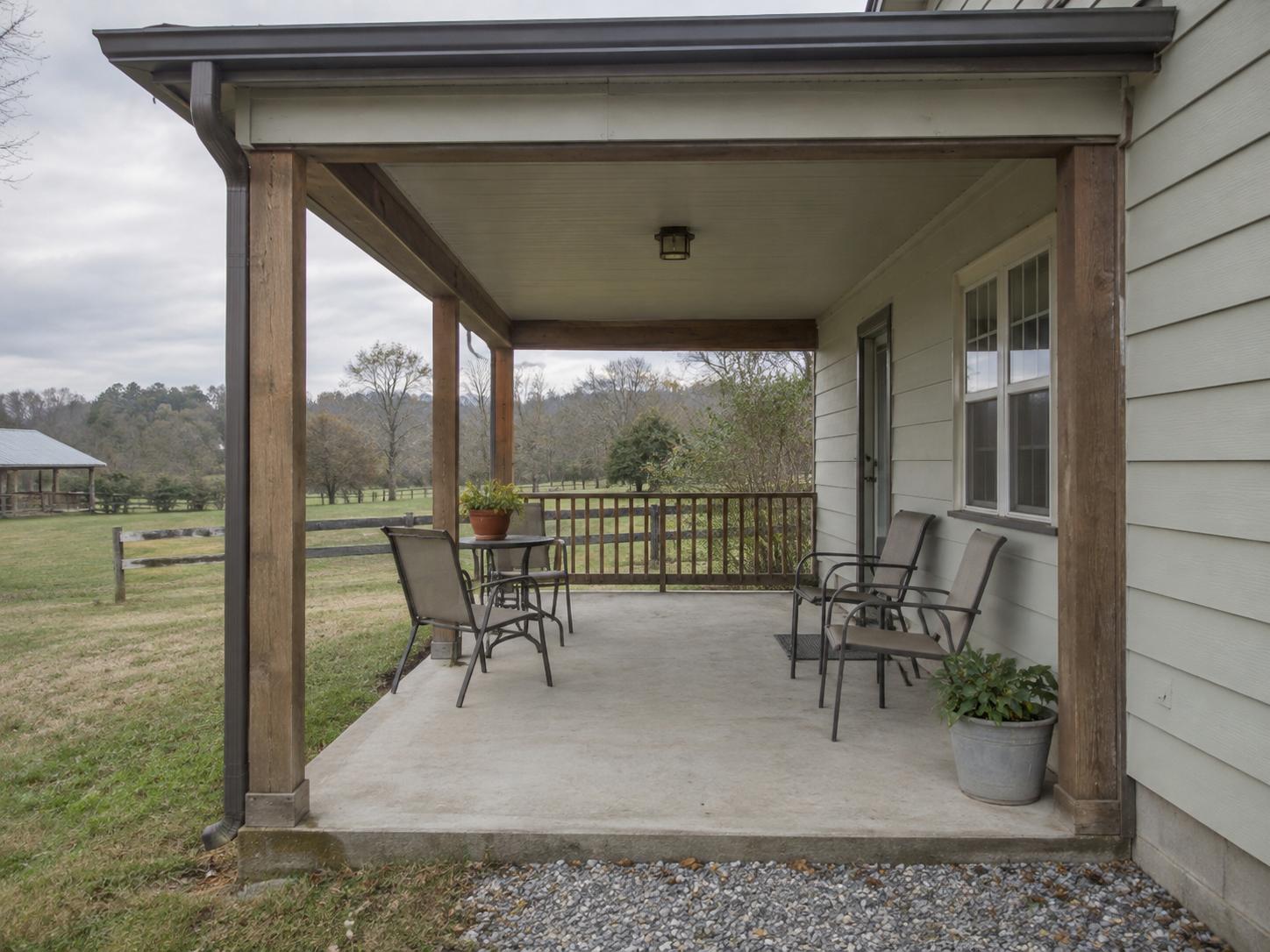 Covered rural cottage patio with concrete slab, wood posts, simple metal chairs and small table