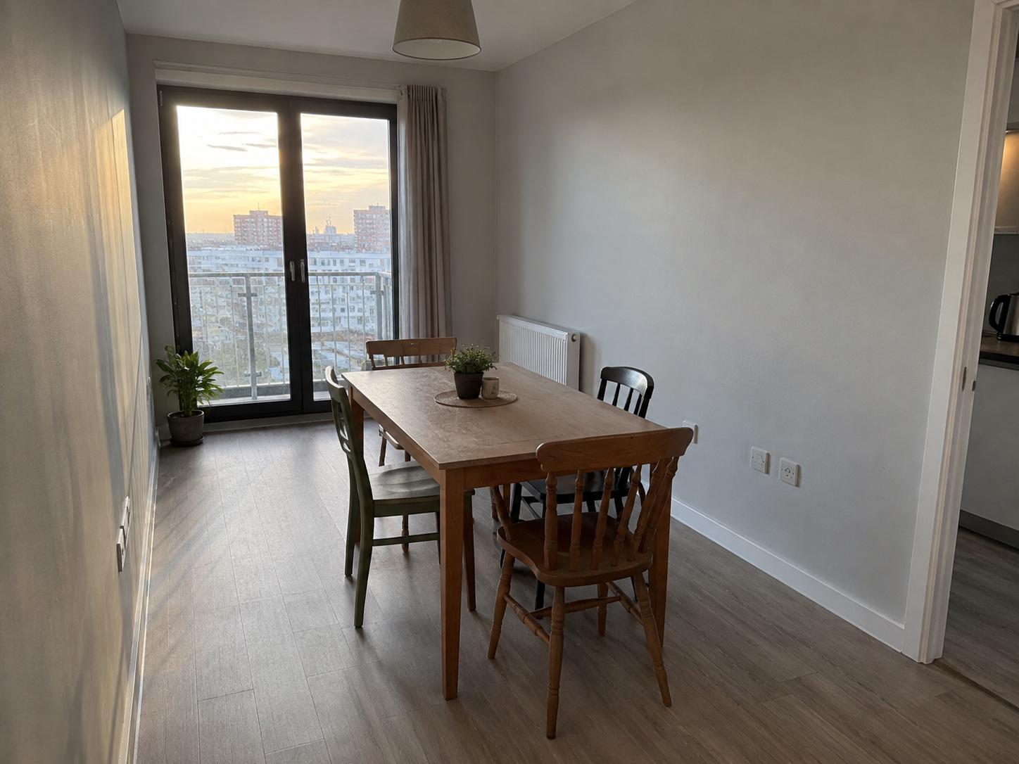 Narrow dining room with wooden table, mixed chairs, balcony doors and a radiator on the right wall