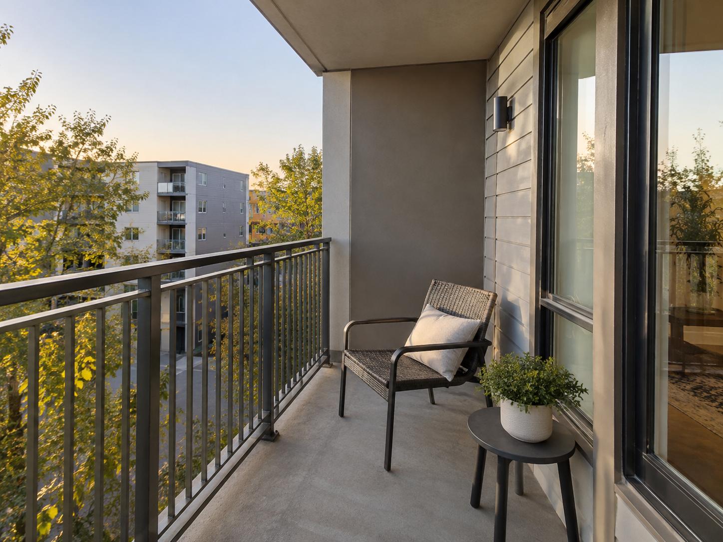 Narrow apartment balcony with metal railing, single woven chair with cushion and small round side table beside sliding window