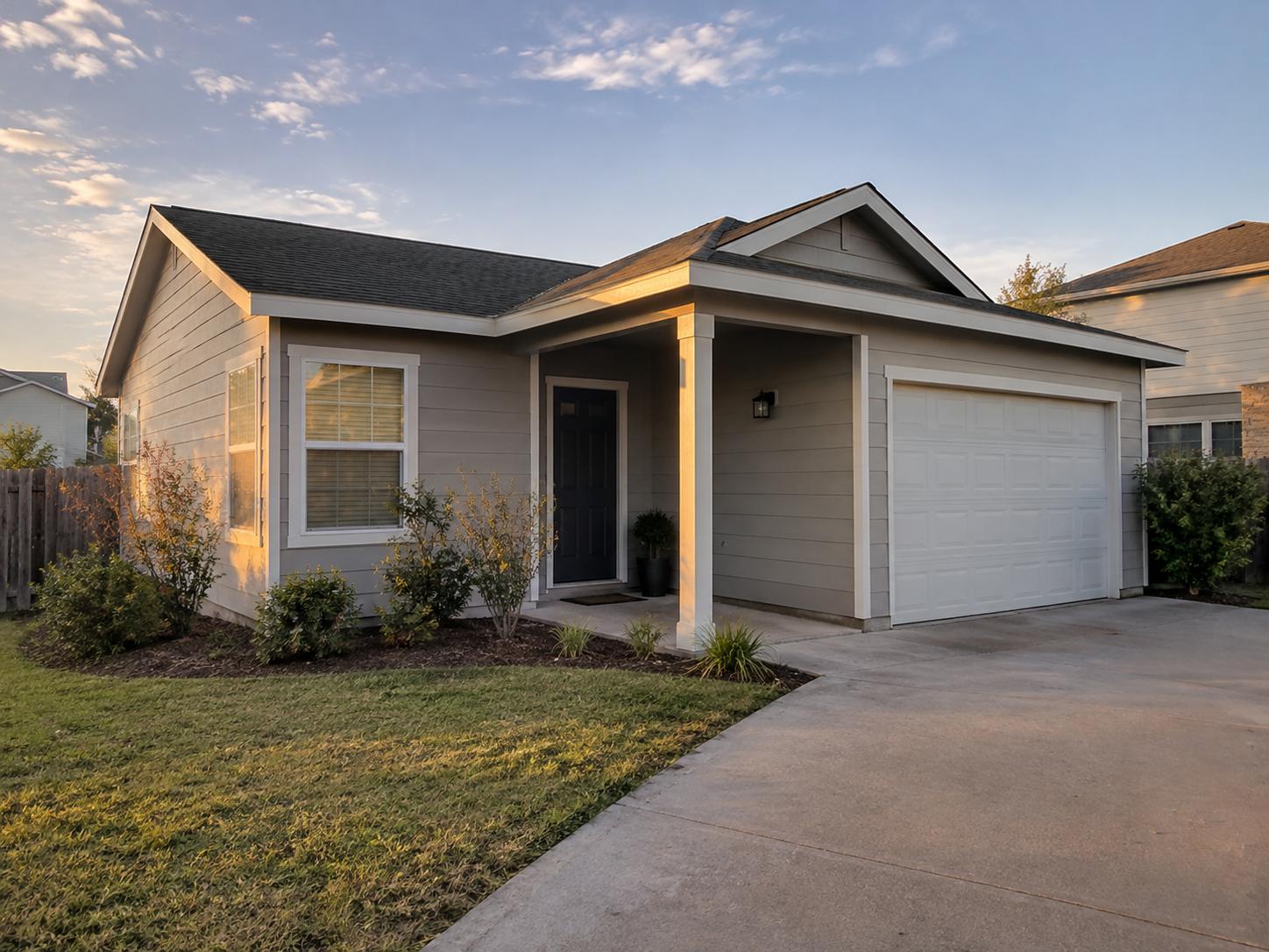 Single-story apartment exterior with light gray horizontal siding, white-trim window and white garage door at sunset