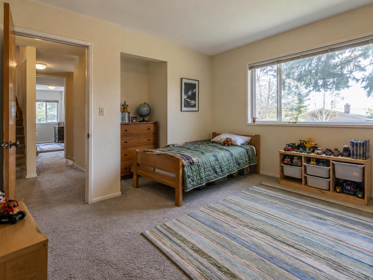 Kids bedroom with single wooden bed, green quilt, toy shelves under window and striped area rug