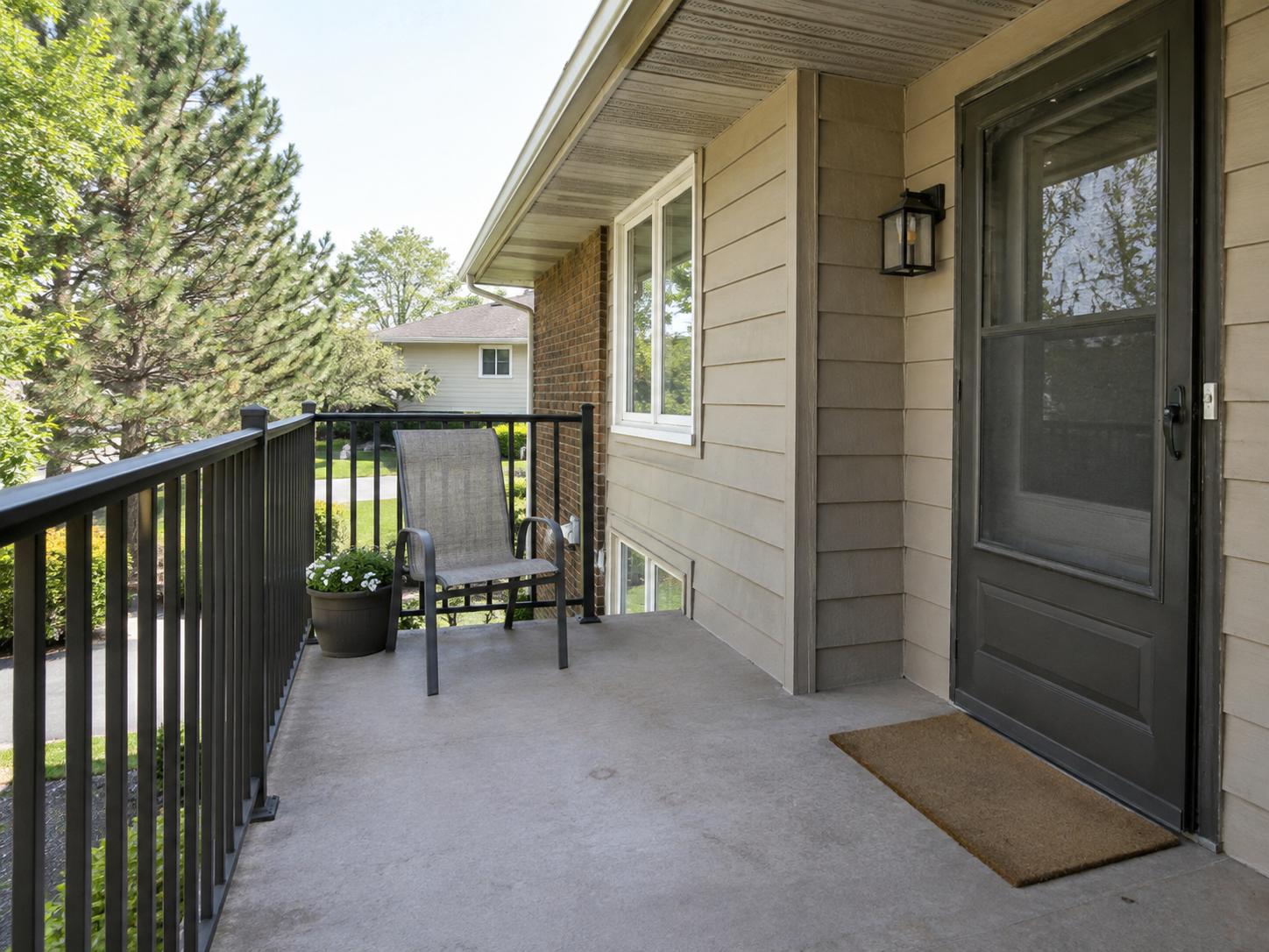 Narrow balcony with black metal railing, single mesh chair, beige siding, exterior screen door and a small potted plant