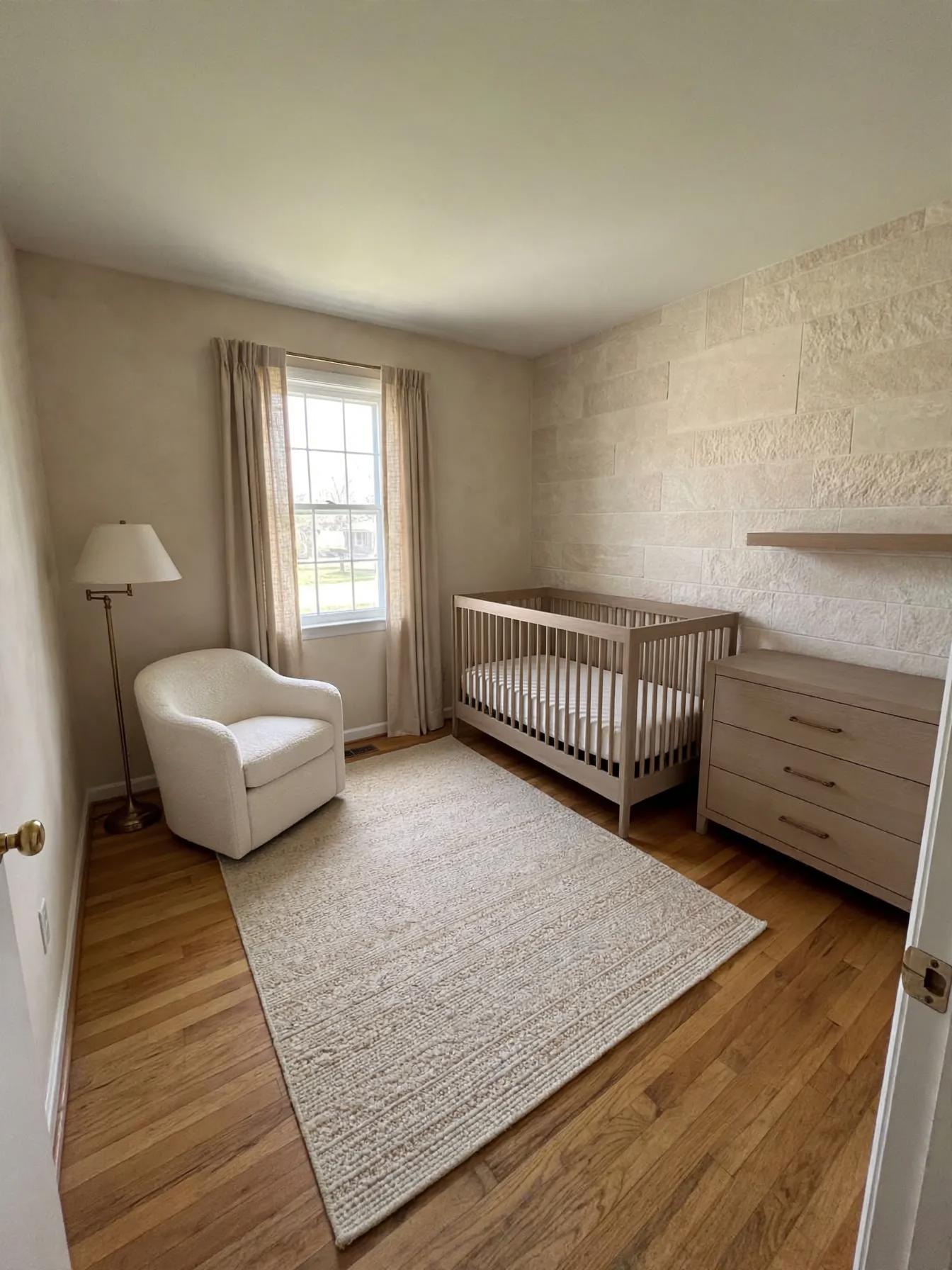 Nursery with textured stone-look accent wall, larger neutral rug, light wood crib and dresser, plush tub chair and floor lamp
