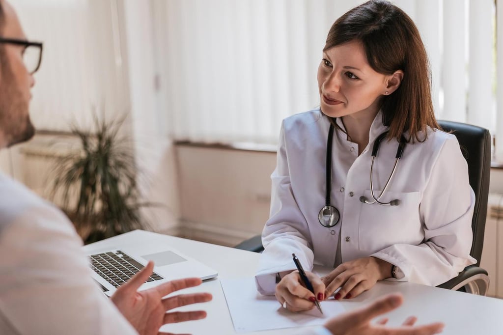 Eine Ärztin mit weißem Kittel und Stethoskop sitzt an einem Schreibtisch und schreibt einem Patienten ein Rezept für Viagra auf.