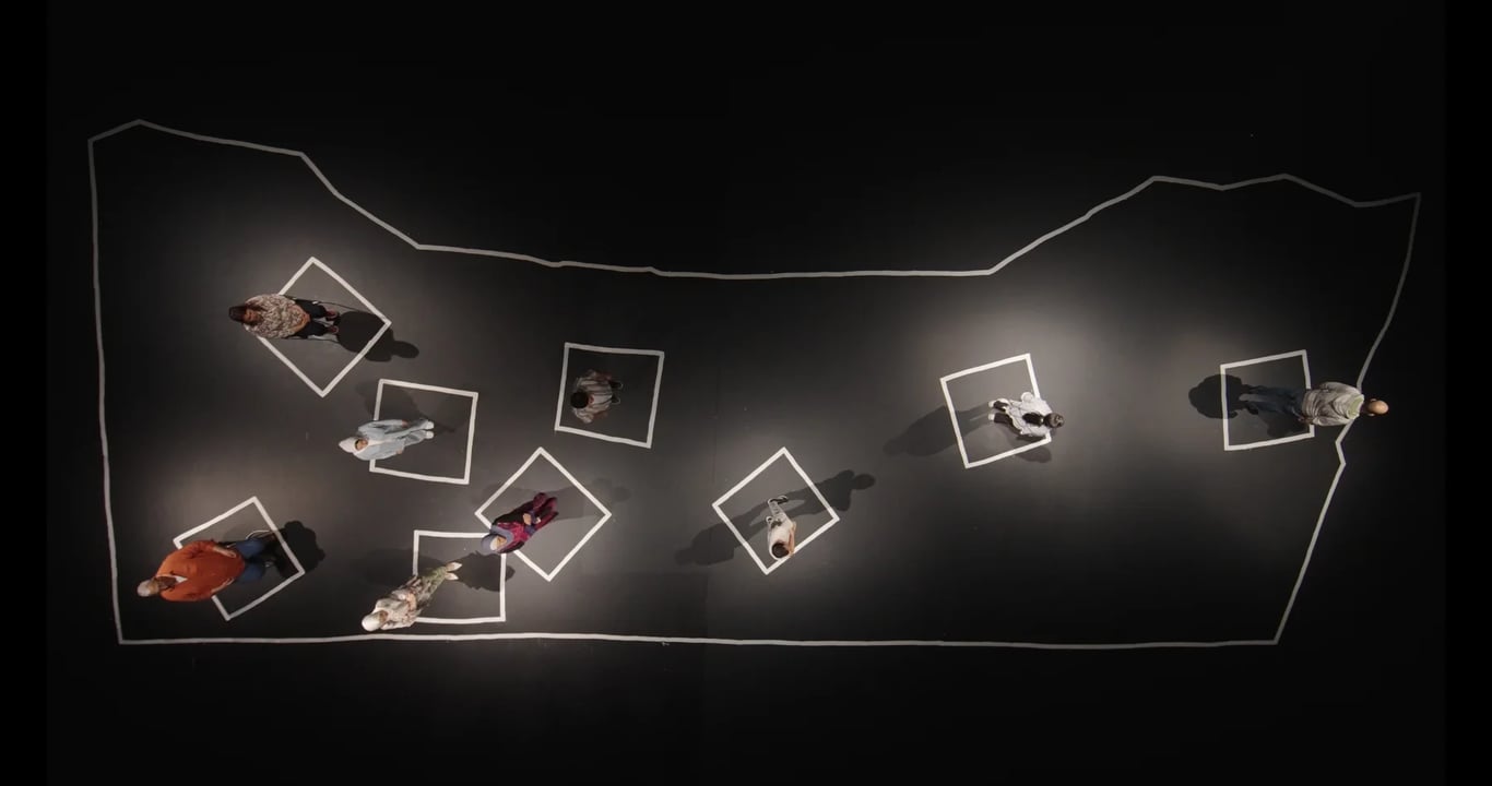 Neuf réfugiés palestiniens se tiennent sur une carte de Gaza dessinée en blanc sur un sol noir dans Qui vit encore de Nicolas Wadimoff.