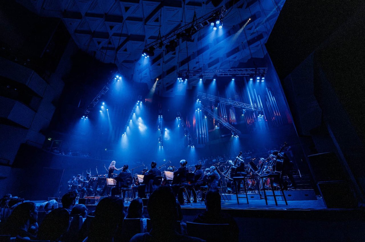 A symphony under blue beams and haze, full lighting rig overhead, a Krank'd production