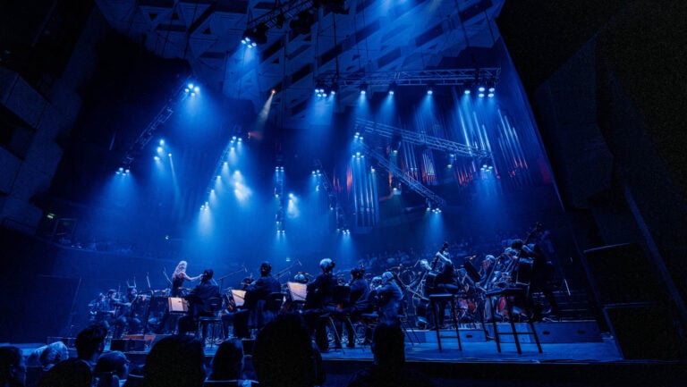 A symphony under blue beams and haze, full lighting rig overhead, a Krank'd production