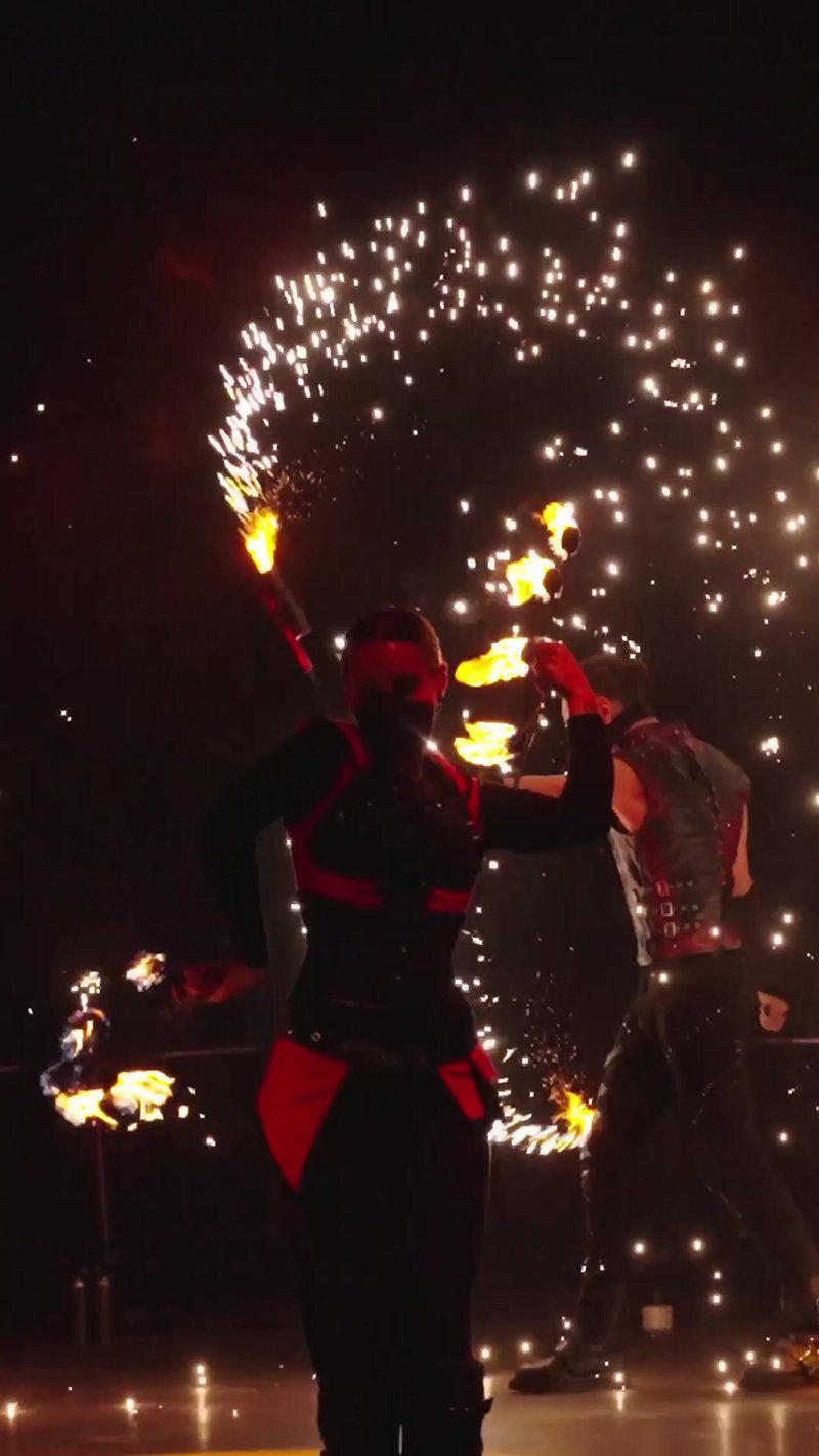 Fire performer mid-routine, sparks arcing under night light