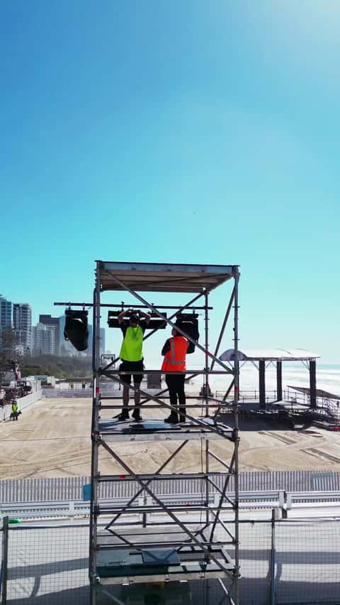 Beach stage build with a crane lowering a wrapped element onto a small stage by the surf
