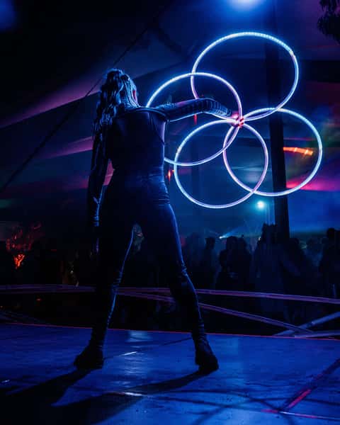 Performer with three LED-lit hoops stacked in front of a festival tent at Dragons Dreaming, deep blue ambient