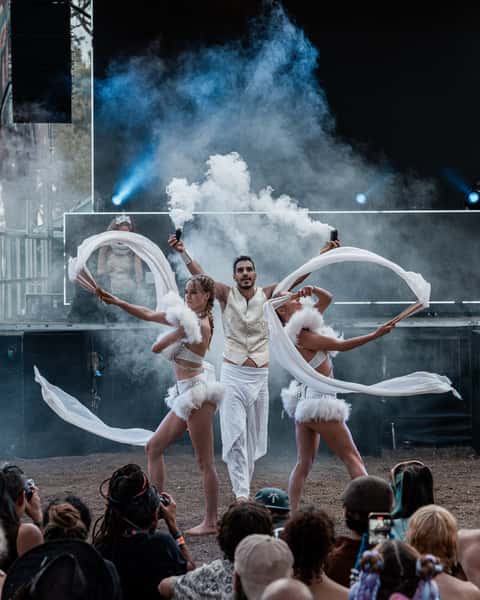 Fan-dance trio on the Earth Frequency festival stage with stage haze and beams