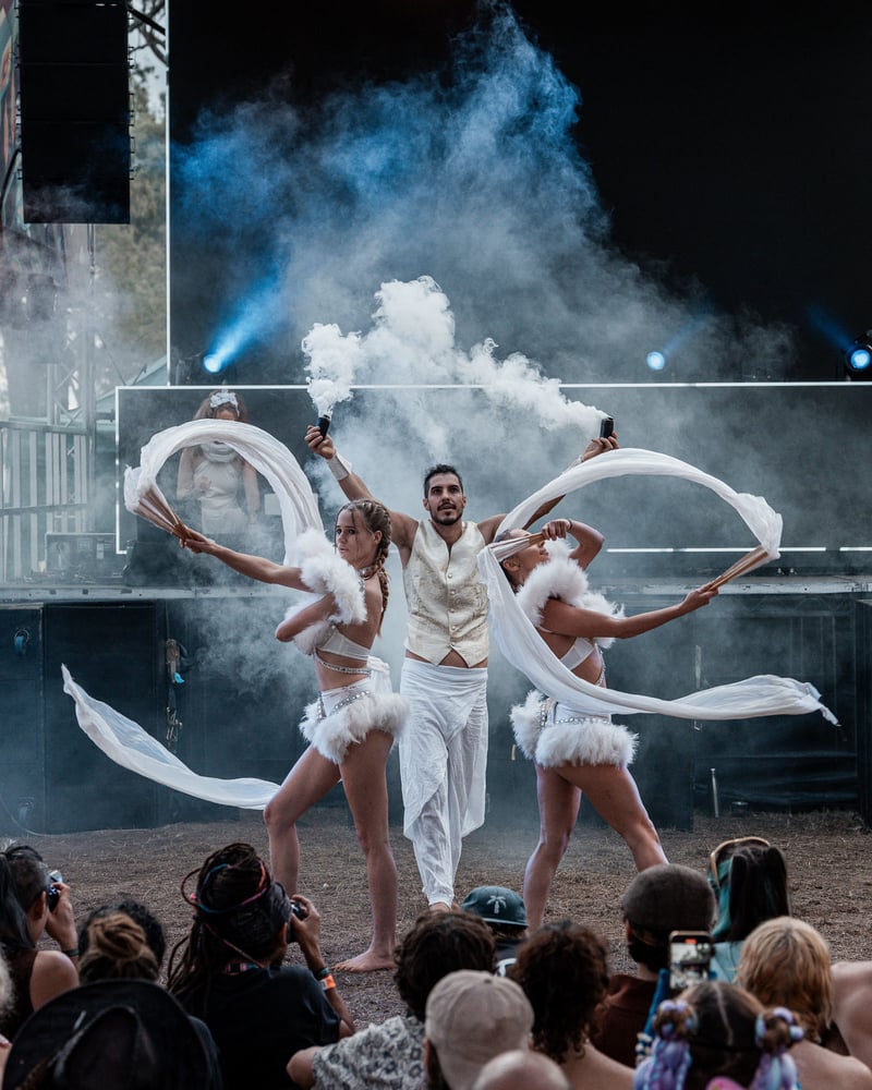 Fan-dance trio on the Earth Frequency festival stage with stage haze and beams